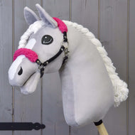 Čierna ohlávka z koženky s ružovým barančekom od Hobby Horse LarDen na svetlosivej plyšovej hlave, s ružovými barančekovými detailmi, bielou priadzovou hrivou a čiernou ohlávkou na drevenej tyči, na pozadí z drevených dosiek.