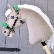Hračka Hobby Horse LarDen s béžovou plyšovou hlavou, bielou priadzovou hrivou a čiernou ohlávkou so zeleným barančekom z koženky na sivo-drevenom pozadí.