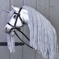 Hobby Horse jednorožec Silver s uzdou a ohlávkou od Hobby Horse LarDen s bielou tvárou, sivou hrivou z priadze, svetlo sivým rohom a čiernou uzdou, nasadený na tyči a odfotografovaný na drevenom pozadí.
