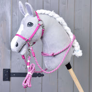 Plyšový sivý Hobby Horse LarDen s bielou hrivou je zobrazený so sadou Set Start Ružový (ohlávka + nákrčník + vodidlo + opraty), upevnený na drevenej tyči na pozadí sivej drevenej steny.