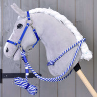 Plyšový sivý Hobby Horse od Hobby Horse LarDen so sadou Set Start modrý (ohlávka + vodidlo + opraty + nákrčník), s modro-bielym vodidlom na drevenej tyči, stojí pred sivou drevenou stenou.