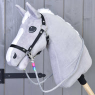 Hobby Horse LarDen Opraty Manhattan, sivý Hobby Horse s bielou hrivou, čiernou ohlávkou, ručne vyrábanými opratami a drevenou tyčou, zobrazený pred sivou drevenou stenou.