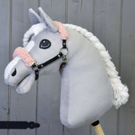 Plyšový Hobby Horse LarDen so sivou tvárou, bielou hrivou a čiernou ohlávkou so staroružovým barančekom z koženky na drevenom pozadí.