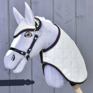 Set Leonardo od Hobby Horse LarDen so sivým plyšovým Hobby Horse s bielou prešívanou dekou, ladiacou čabrakou, čiernou uzdečkou a opratami na drevenej tyči, zobrazený na pozadí sivej drevenej steny.