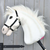 Hobby Horse Nexus s čiernou ohlávkou od Hobby Horse LarDen, biely plyšový športový kôň s huňatou hrivou, veľkým gombíkovým okom a čiernou ohlávkou, odfotografovaný pred sivou drevenou stenou – ideálny pre každého nadšenca.