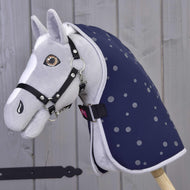 Sivý plyšový Hobby Horse od Hobby Horse LarDen s čiernou uzdečkou a Dekou stajňovou Night Sky, nasadený na drevenej tyči na pozadí svetlej drevenej steny.
