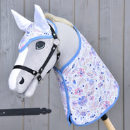 Hobby Horse LarDen Set Vanessa NEW so sivým Hobby Horse, čiernou uzdečkou, kvetinovou súpravou dečky s modrým lemom a ladiacou čabrakou, všetko zobrazené na drevenom pozadí.