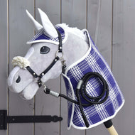 Set Cube (čabraka, deka, ohlávka s barančekom, vodidlo) od Hobby Horse LarDen s dekou, čabrakou, vodidlom a ohlávkou s barančekom, vystavený na drevenej stene pri čiernom pánte brány. Doplnky zdôrazňujú kvalitu a čaro produktov Hobby Horse LarDen.