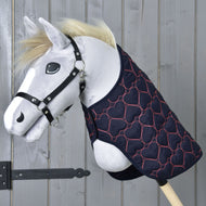 Plyšový Hobby Horse s čiernou ohlávkou a prešívanou dekou Pink Heart od Hobby Horse LarDen, zdobenou ružovými srdcami, na drevenom pozadí