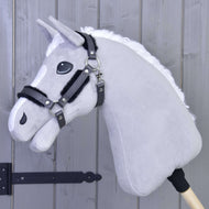 Ohlávka s barančekom z koženky Graphite Full od Hobby Horse LarDen na drevenej tyči, opretá o svetlosivú drevenú stenu, so sivou plyšovou hlavou s bielou hrivou, čiernou uzdečkou a ohlávkou z koženky.