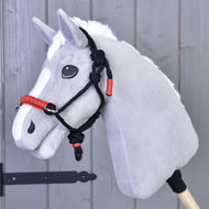 Sivý plyšový Hobby Horse s bielou hrivou v čiernočervenej parelke pred sivou drevenou stenou