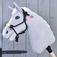 Sivý plyšový Hobby Horse s bielou hrivou v čiernej parelke s dúhovým nánosníkom pred sivou drevenou stenou
