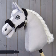 Čierna ohlávka z koženky s kompletným čiernym barančekom od Hobby Horse LarDen na drevenej tyči, zobrazená pred dreveným obkladom.