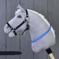 Hobby Horse nákrčník modrý (veľ. S) od Hobby Horse LarDen na sivom plyšovom Hobby Horse s bielou hrivou, čiernou uzdečkou a modrofialovou stuhou na drevenej tyči, pred sivou drevenou stenou.