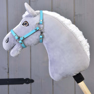 Sivý plyšový Hobby Horse s bielou hrivou a modrou uzdečkou má na sebe Ohlávku čiernu z koženky (veľ. S) od Hobby Horse LarDen, na drevenej tyči pred sivými drevenými panelmi.