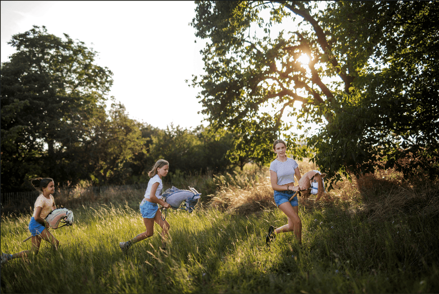Deti bežia s Hobby Horses cez slnečnú trávnatú lúku