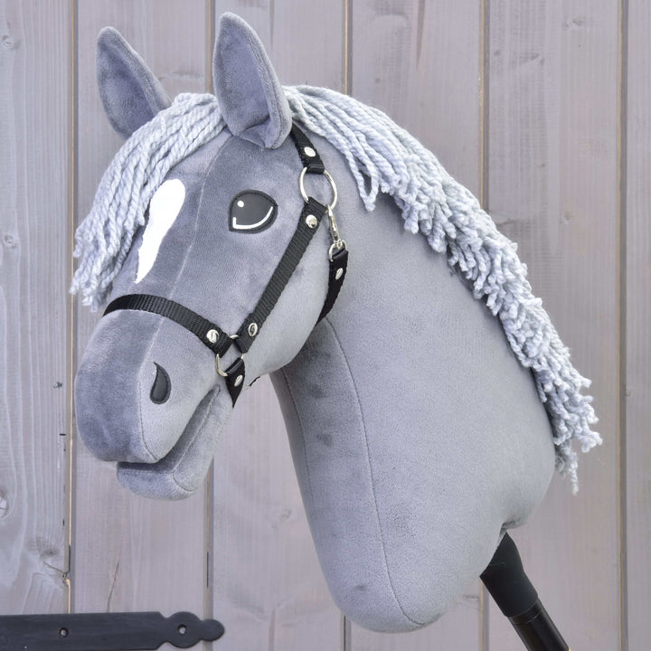 Sivý Hobby Horse s bielou škvrnou na čele, čiernou uzdečkou a hrivou z priadze, na drevenom pozadí.