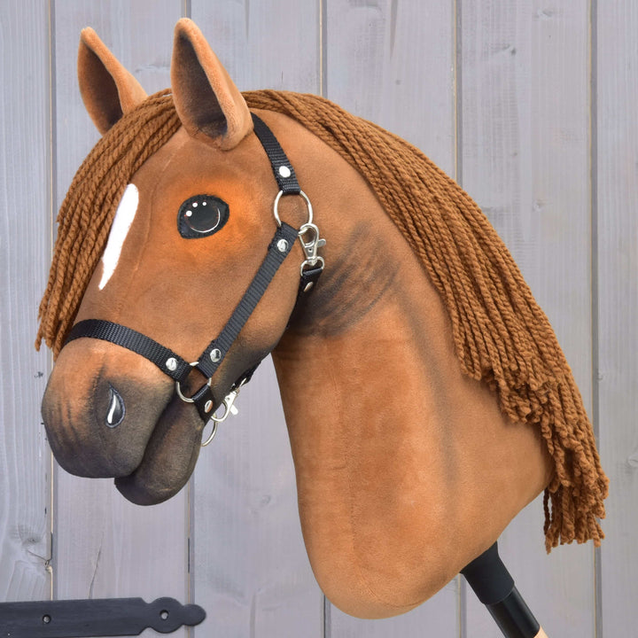 Realistický Hobby Horse s hnedou plyšovou hlavou, čiernou uzdečkou, bielou lysinou na čele a dlhou hrivou z priadze, umiestnený pred svetlou drevenou stenou.