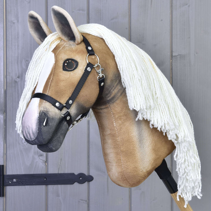 Realistický Hobby Horse palomino so svetlohnedou tvárou, bielou lysinou, čiernou uzdečkou a dlhou bielou hrivou z priadze, vystavený pred sivou drevenou stenou.