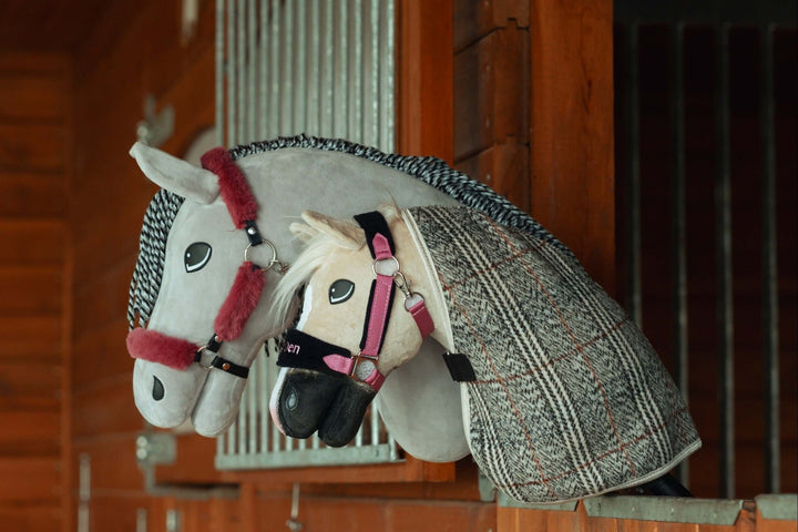 Dva plyšové Hobby Horse s uzdečkami a dečkami odpočívajú na drevenej priečke stajne a pripomínajú skutočné kone v boxe. Ideálne pre fanúšikov Hobby Horsingu, biely a sivý kôň majú prepracované detaily a výstroj.