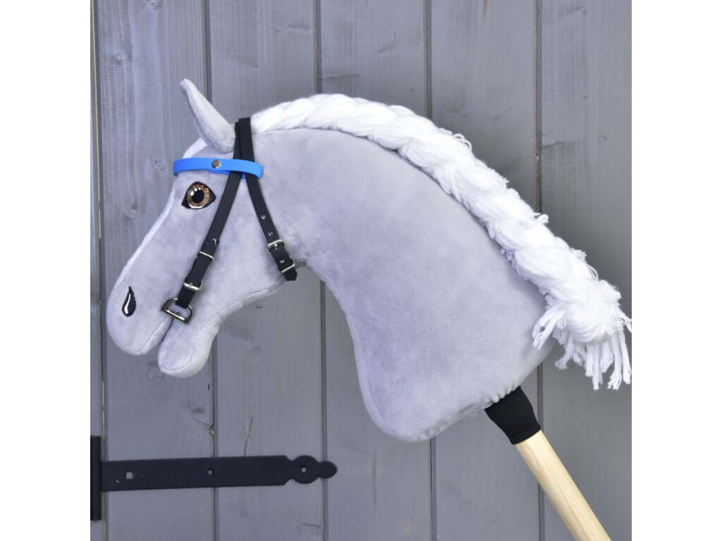 Uzdečka s čelenkou bez nánosníka modrá (veľ. S) od Hobby Horse LarDen na sivom Hobby Horse s bielou priadzovou hrivou, nasadenom na drevenej tyči pred sivými drevenými dverami.