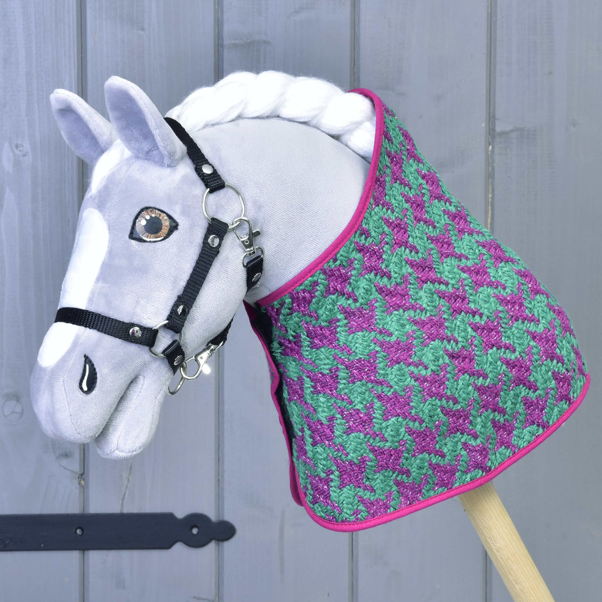 Set Coco od Hobby Horse LarDen: sivý Hobby Horse s čiernou uzdečkou, vo fialovo-zelenom sete deky so vzorom kohútej stopy, ružovým lemom a čabrakou na uši, pred sivou drevenou stenou.