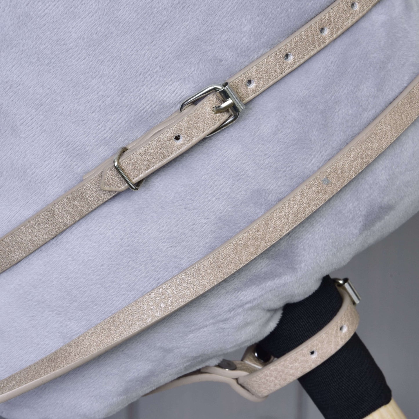 Detail béžových remienkov z koženky Bordeaux s kovovými prackami zo setu uzdečky, oprát a martingalu od Hobby Horse LarDen, upevnených cez mäkký svetlosivý plyšový povrch.