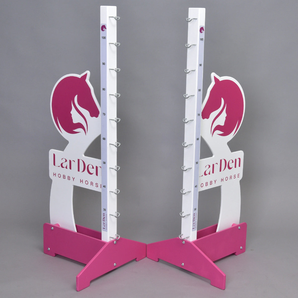 Dva stojany Prekážka LarDen kolmák 110 cm od Hobby Horse LarDen v ružovej a bielej farbe s motívmi konských hláv, značkami nastaviteľnej výšky a kovovými držiakmi na tyče stoja na sivom pozadí. Na základni je vytlačené „LarDen HOBBY HORSE“.