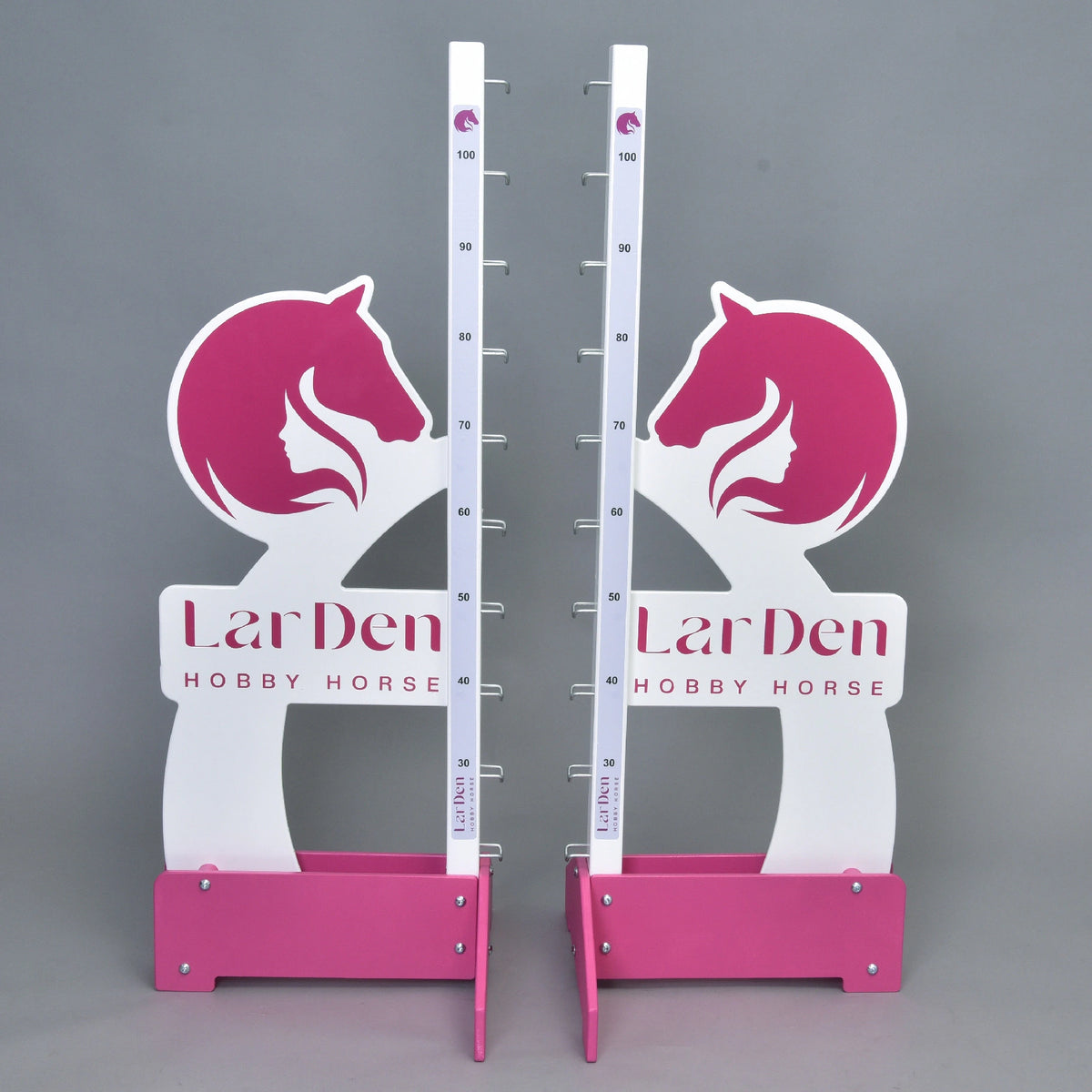Dva biele a ružové stojany Prekážka LarDen kolmák 110 cm od Hobby Horse LarDen s nastaviteľnou výškou až do 110 cm, grafikou konskej hlavy a textom značky na základni — ideálne pre jazdu na Hobby Horse, zobrazené na jednofarebnom sivom pozadí.