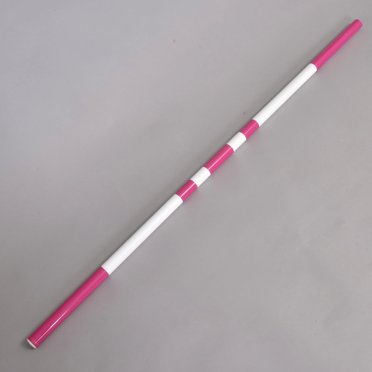 Prekážka LarDen kolmák 110 cm od Hobby Horse LarDen so striedajúcimi sa ružovými a bielymi segmentmi leží diagonálne na svetlosivom povrchu — ideálna pre nadšencov do jazdy na Hobby Horse.