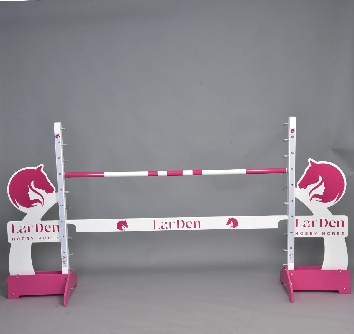 Prekážka LarDen kolmák 110 cm od Hobby Horse LarDen s ružovými a bielymi tyčami, siluetami konských hláv a nastaviteľnou výškou — ideálna pre jazdu na Hobby Horse. Značka: Hobby Horse LarDen. Na jednofarebnom sivom pozadí.