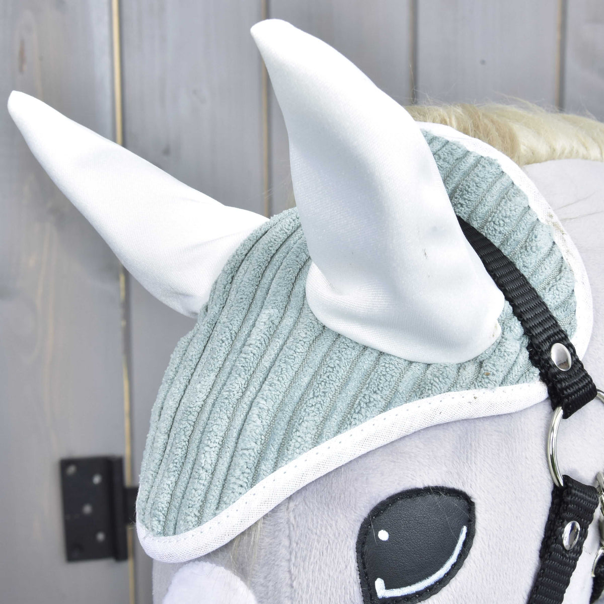 Detail Set Manchester Little Green od Hobby Horse LarDen: plyšová konská hlava s textúrovanou svetlosivou čabrakou na uši, veľkými bielymi ušami, čiernou uzdečkou a vyšívaným okom na drevenom pozadí.