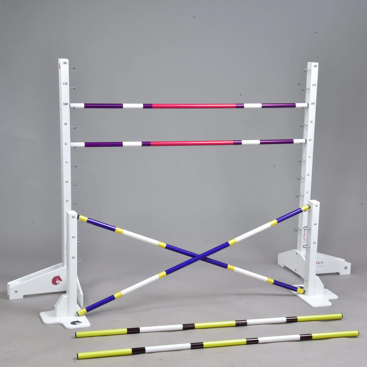 Set prekážok pre Hobby Horsing od Hobby Horse LarDen zahŕňa biele stojany s meracími značkami, štyri farebné tyče (dve vodorovné a dve skrížené) a vpredu dve žlto-čierne cavaletti, zobrazené na jednofarebnom sivom pozadí.