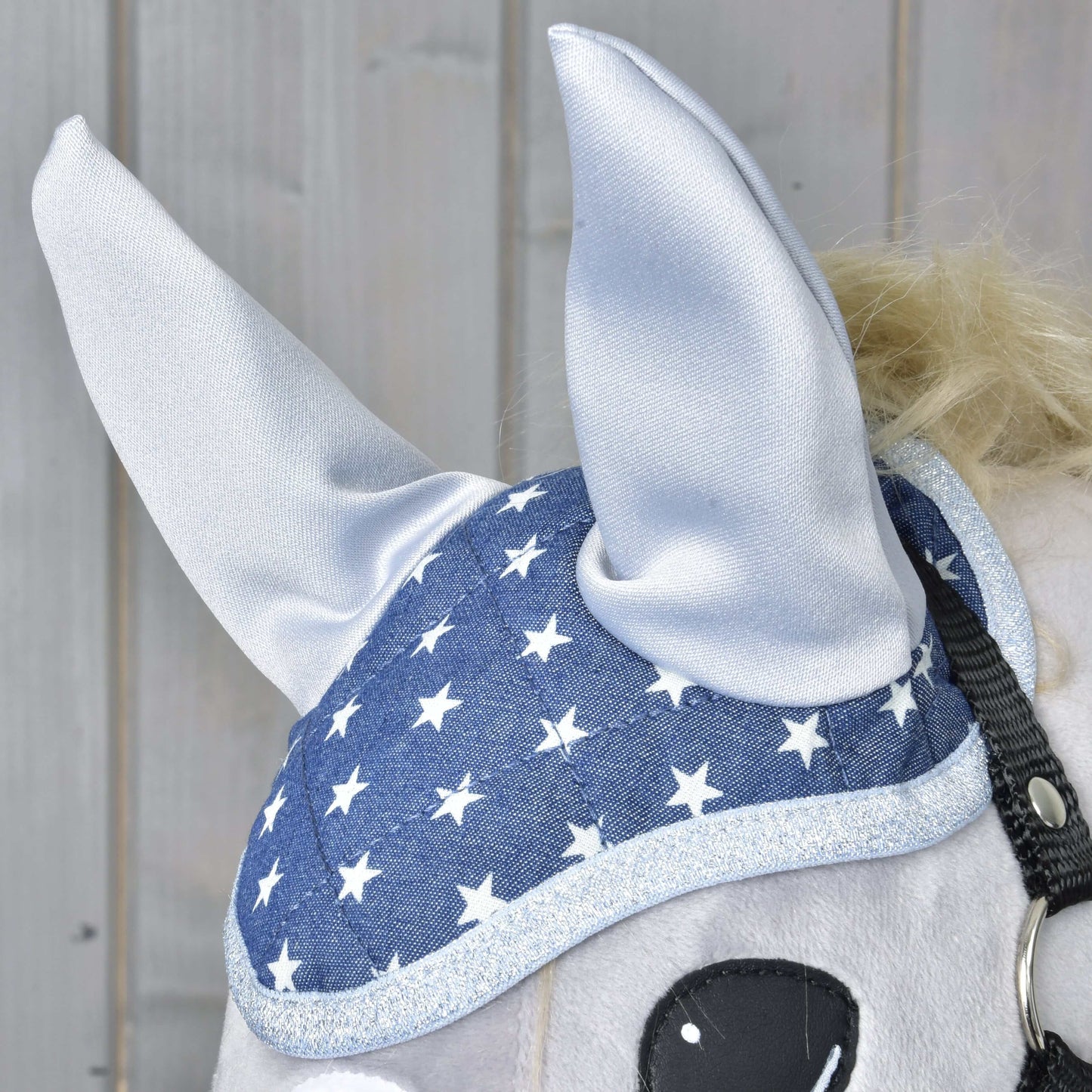 Detail koňa s čabrakou Čabraka Star od Hobby Horse LarDen, s modrým dizajnom s bielymi hviezdami a strieborným lemovaním pre štýlovú ochranu proti hmyzu. Časť oka koňa vidno na pozadí zo svetlých drevených panelov.