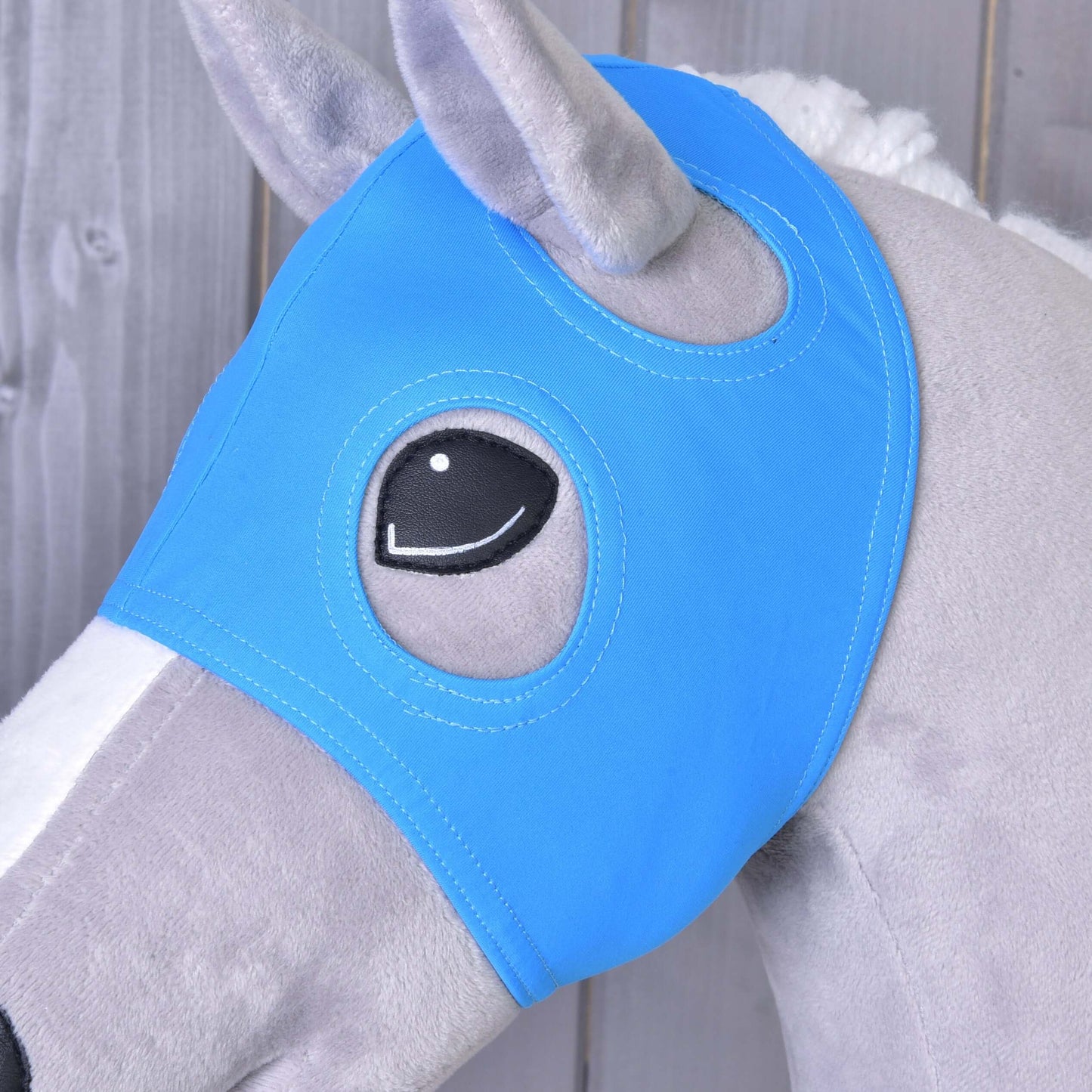 Detail šedého hračkového koně s Maskou bez uší Sky od Hobby Horse LarDen, s otvory pro oči, na dřevěném pozadí.