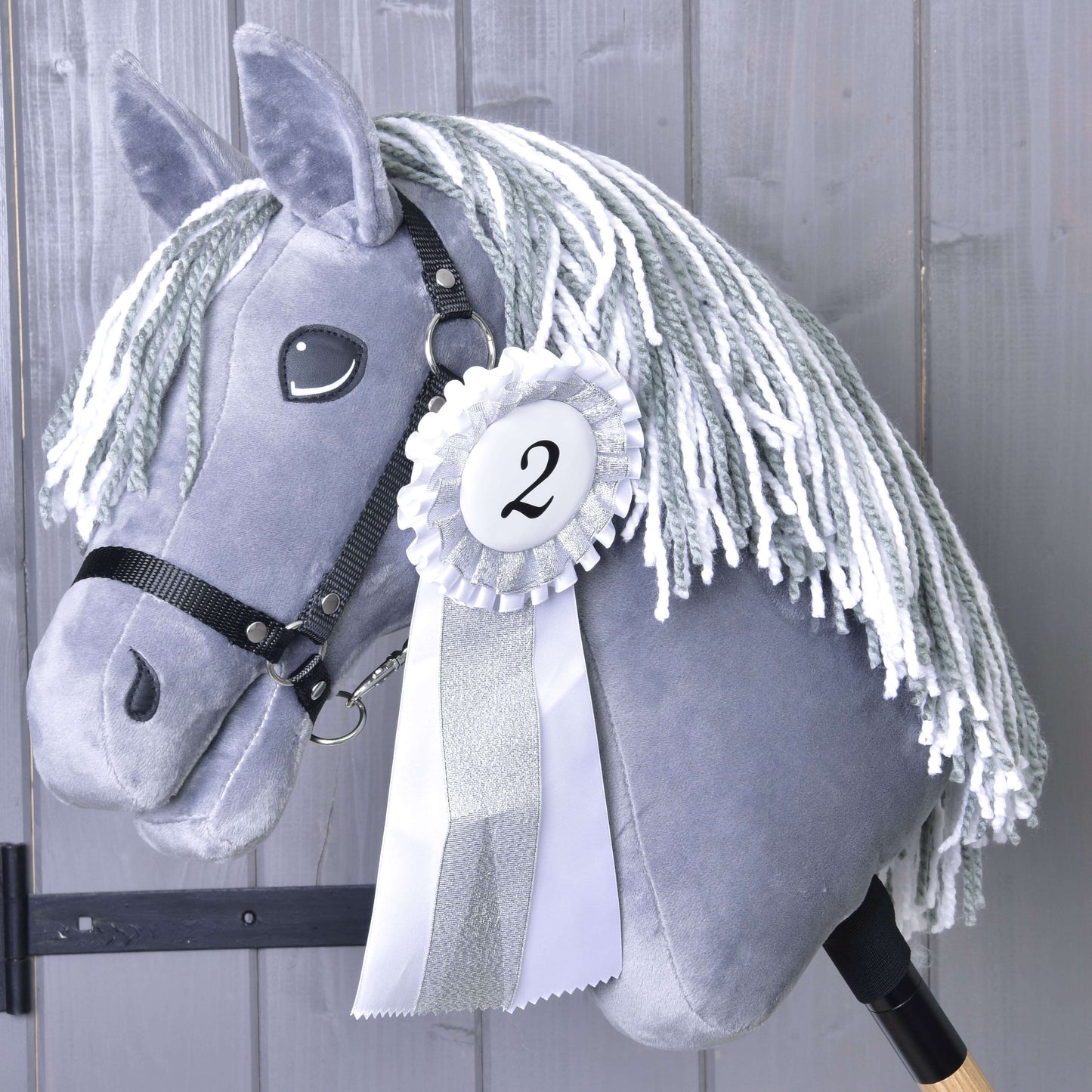 Sivý Hobby Horse s bielou priadzovou hrivou a čiernou uzdečkou na drevenej tyči má Set Hobby Horse Kokarda NEW (druhé miesto, strieborné lemovanie, číslo 2) od Hobby Horse LarDen na pozadí sivých drevených dosiek.