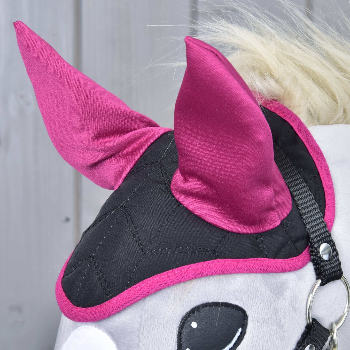 Detail čabraky Thermo Sky od Hobby Horse LarDen v čiernej a magentovej farbe s dvoma špicatými magentovými ušami a prešívaným vzorom, poskytujúcej ochranu proti hmyzu, na svetlom drevenom pozadí.