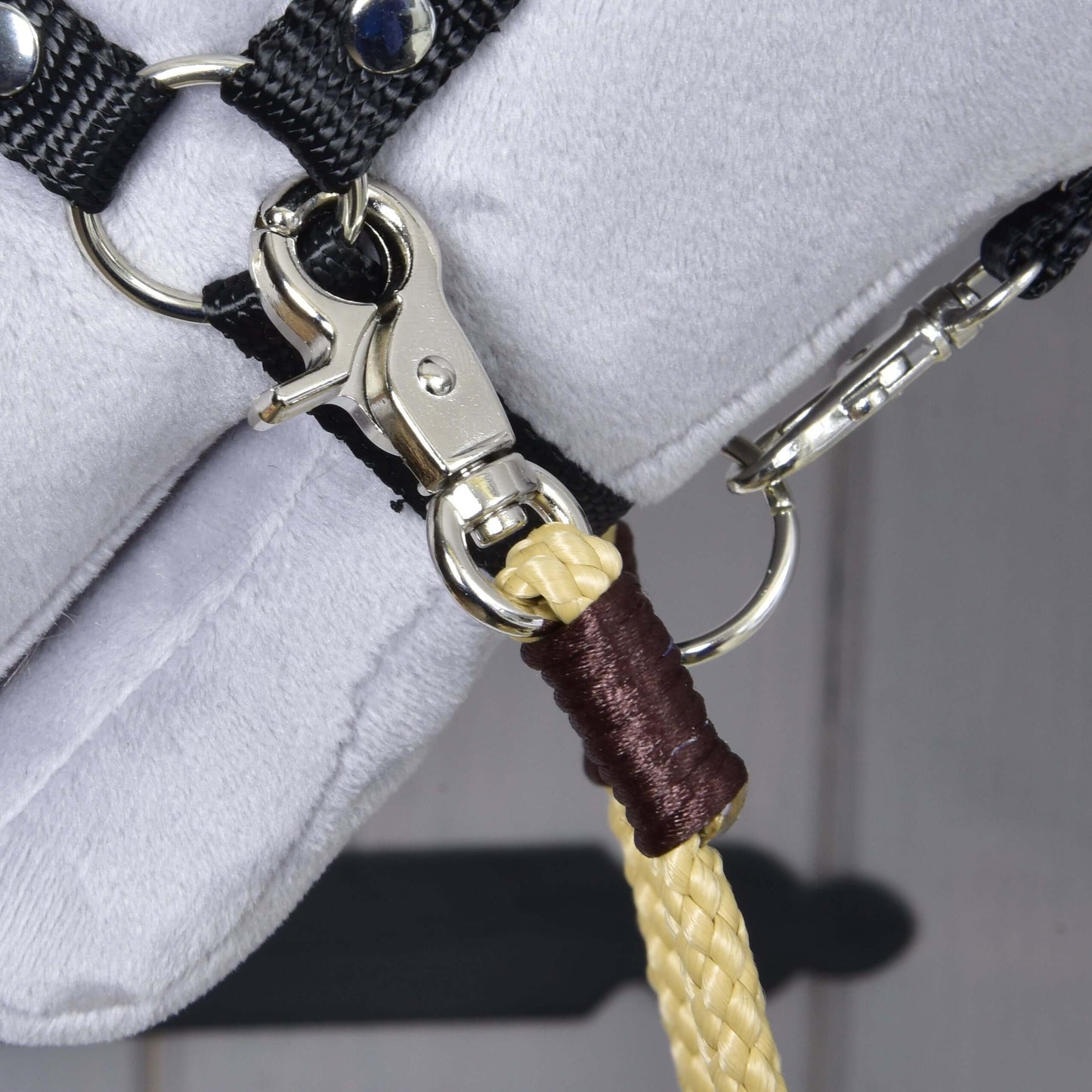 Detail kovovej karabíny na čiernom remienku s pleteným žltým lanom upevneným hnedou niťou – ideálny na tréning s Westernovými opratami Dakota od Hobby Horse LarDen na bielom povrchu.
