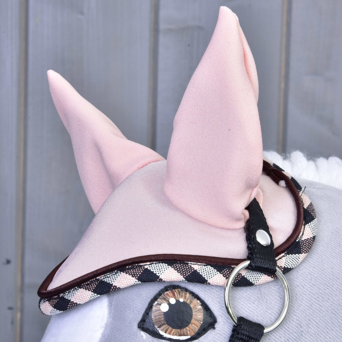 Detail plyšovej hračky Set Abby od Hobby Horse LarDen s ružovou čabrakou na uši s károvaným lemovaním a čiernym pásikom. Na drevenom pozadí vidno veľké látkové uši a prešité oko.