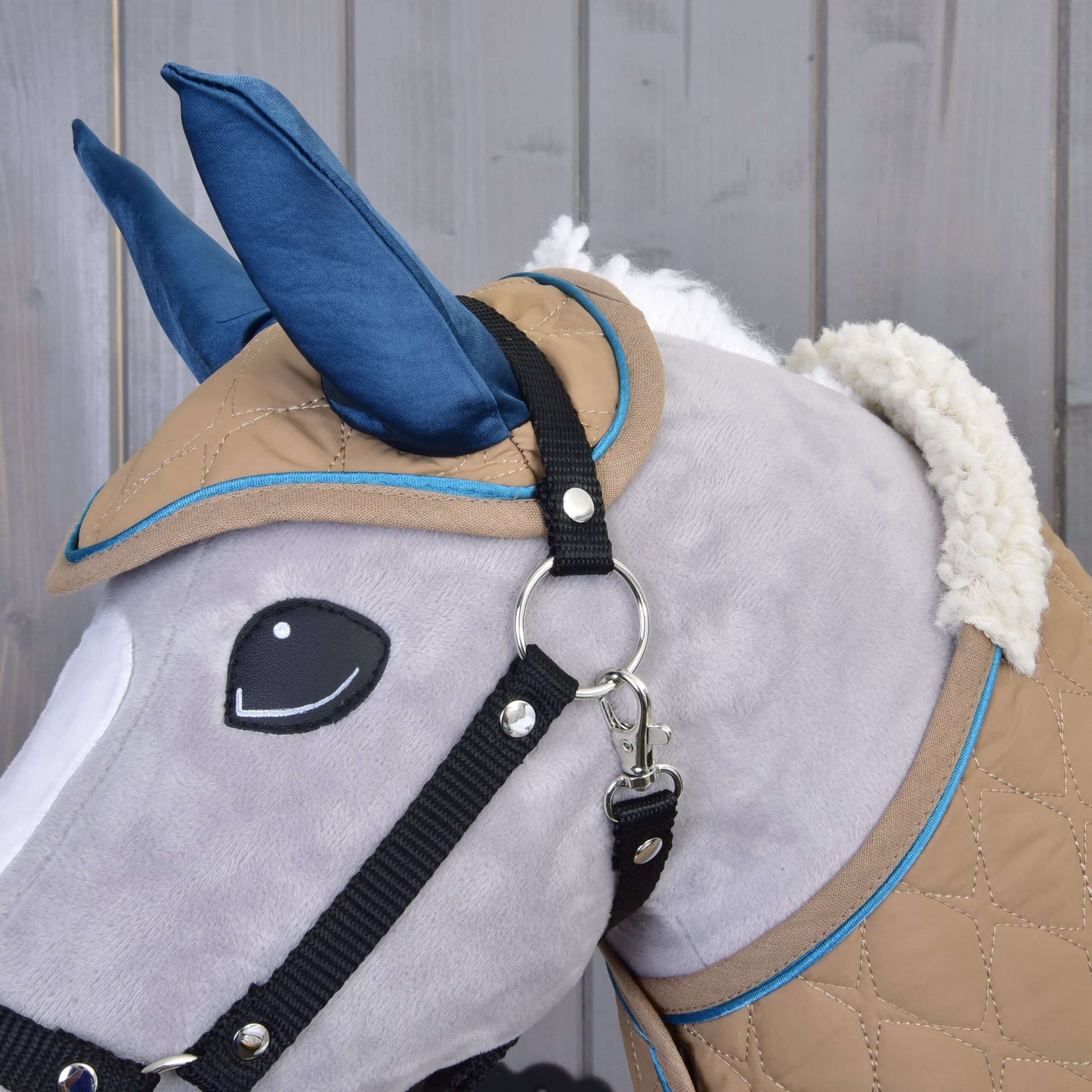 Detailní záběr na Set Almond Star od Hobby Horse LarDen – šedý plyšový Hobby Horse s modrými ušima, černou uzdečkou a béžovo-modrým prošívaným potahem – na dřevěném pozadí.