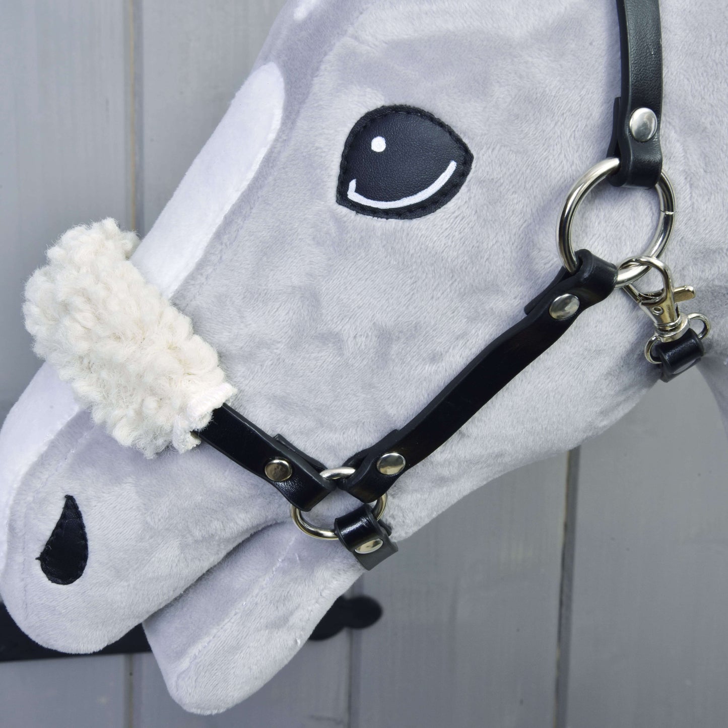 Detail sivej hlavy Set Basic Hobby Horse od Hobby Horse LarDen s čiernou uzdečkou s opratami a bielym chlpatým nánosníkom na svetlom drevenom pozadí.