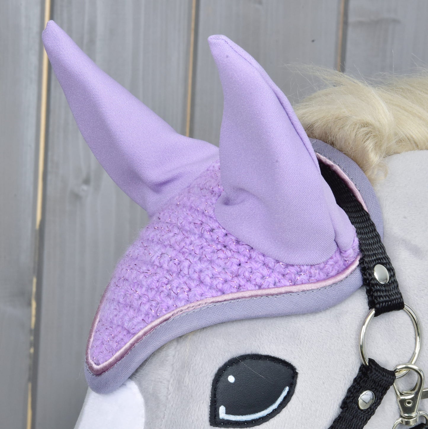 Detail sivej plyšovej hračky koňa od Hobby Horse LarDen s Čabraka Orchid pre ochranu pred hmyzom a s čiernou uzdečkou, na drevenom pozadí.
