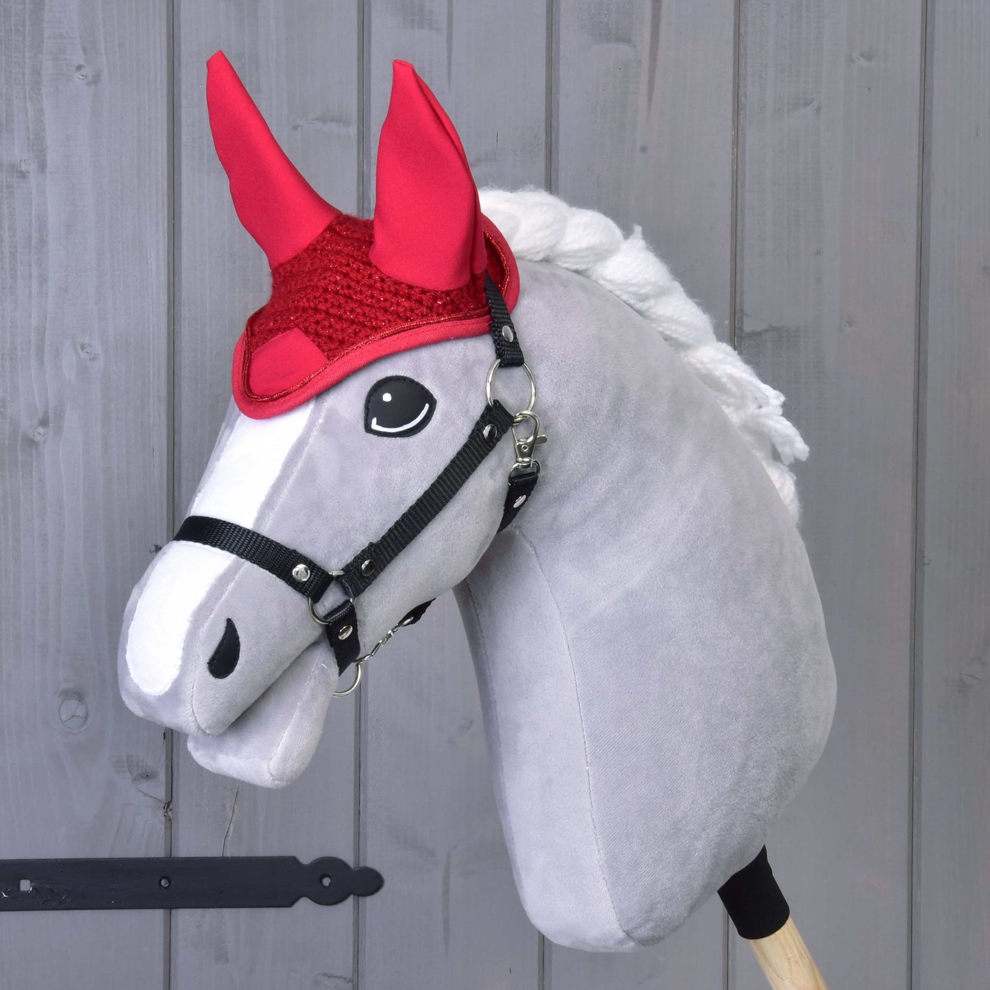Sivý Hobby Horse od Hobby Horse LarDen s bielou hrivou, čiernou uzdečkou a čabrakou Čabraka háčkovaná červená na ochranu proti muchám, pred svetlým dreveným pozadím.