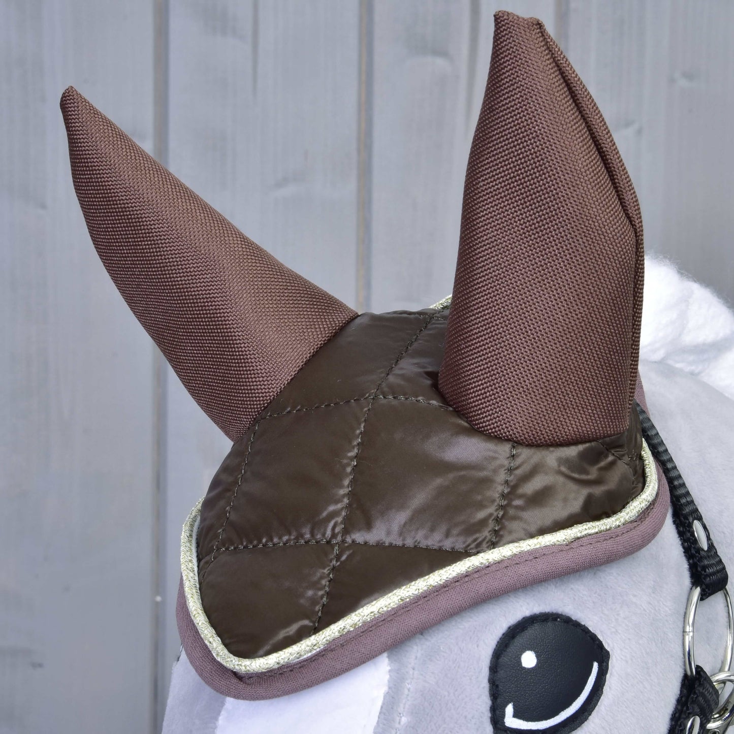 Detail Set Thermo Chocolate od Hobby Horse LarDen s velkými látkovými ušima a prošívanou hnědou čabrakou se světlým lemem, jako půvabná dekorace koně před šedým dřevěným pozadím.