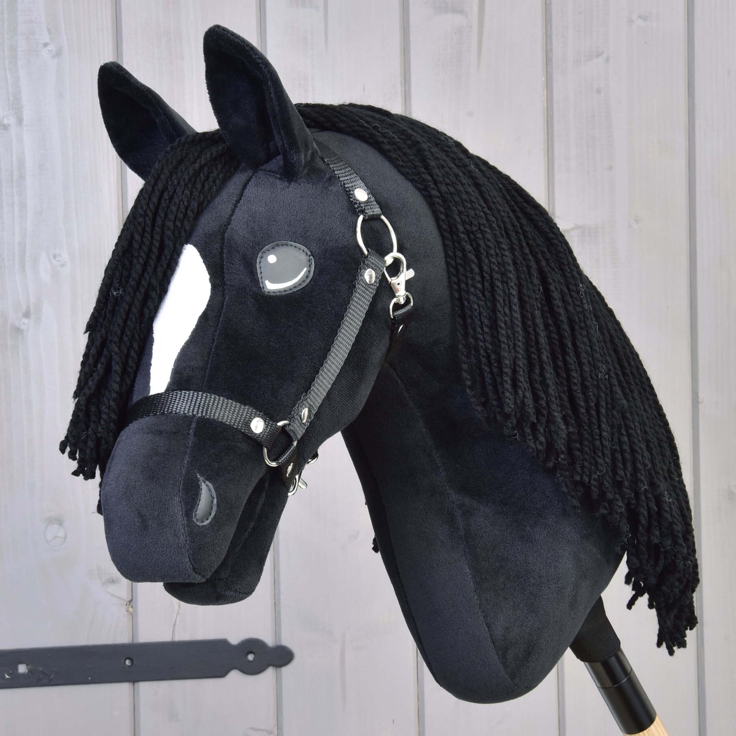 Hobby Horse Cloony s čiernou ohlávkou od Hobby Horse LarDen, plyšový žrebec American Quarter Horse z čiernej látky s bielou škvrnou na hlave, gombíkovými očami, čiernou priadzovou hrivou a uzdečkou na svetlom drevenom pozadí.
