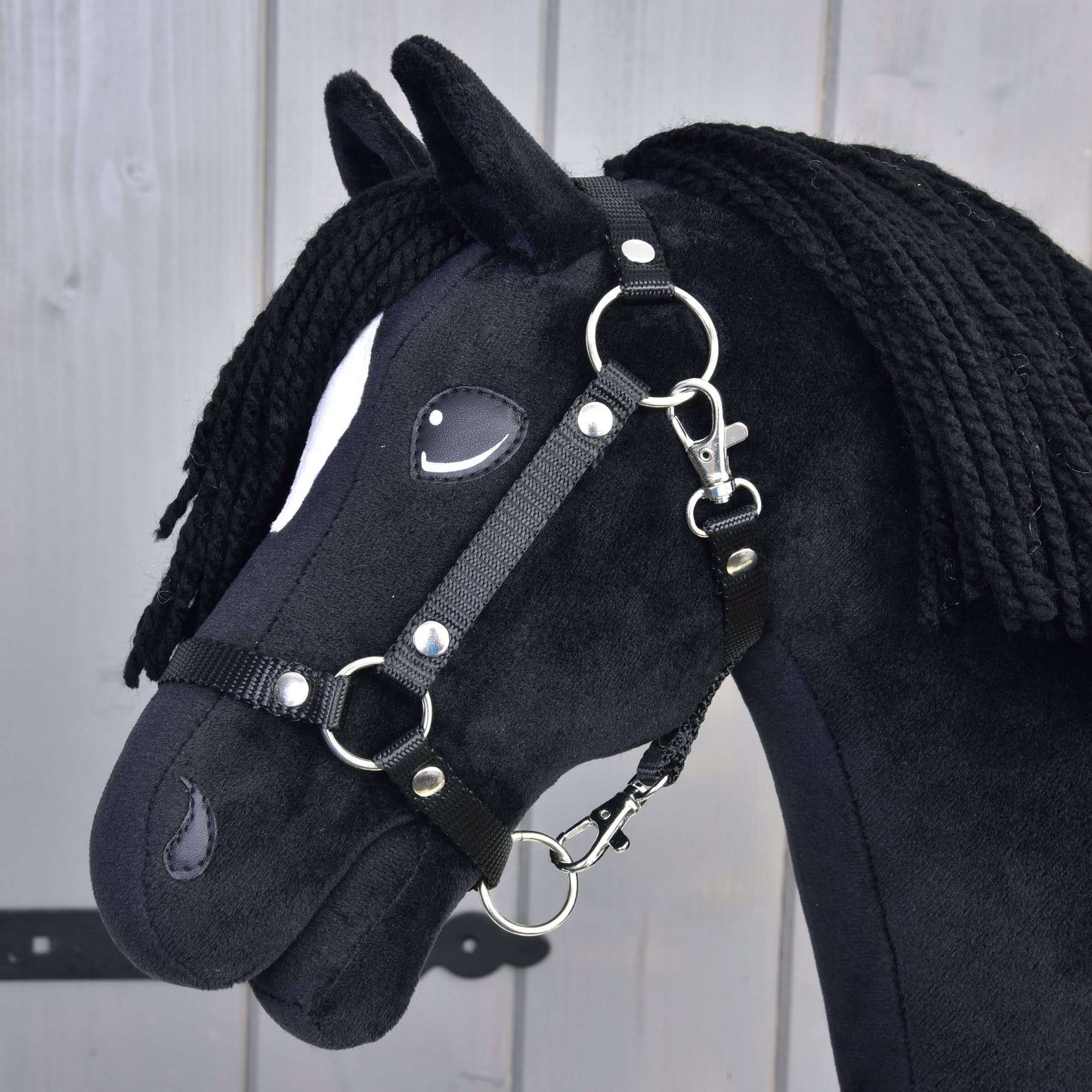 Hobby Horse Cloony s čiernou ohlávkou od Hobby Horse LarDen, čierny látkový kôň v štýle žrebca American Quarter Horse, s bielou škvrnou pri oku, čiernou priadzovou hrivou, odfotografovaný na svetlom dreve.