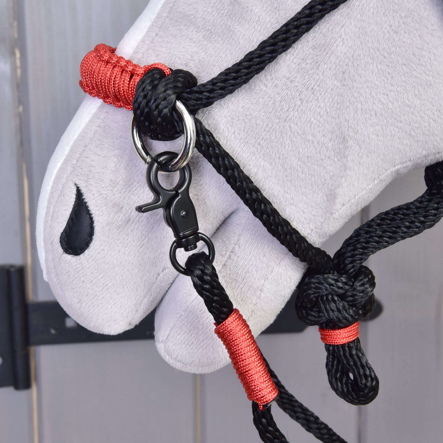 Detail hlavy bieleho plyšového koňa s ohlávkou Hobby Horse LarDen Povrazový set Spark s červeným omotaním a kovovou karabínou, s čiernym znakom v tvare slzy pri oku.