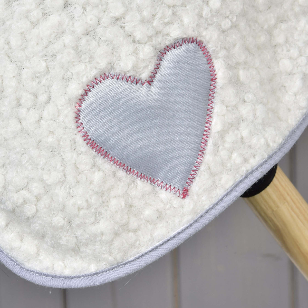 Detail bielej textúrovanej čabraky Set Snowflake od Hobby Horse LarDen s lesklou svetlosivou nášivkou v tvare srdca a ružovým cikcak stehom; v pravom dolnom rohu vidno drevenú tyč.
