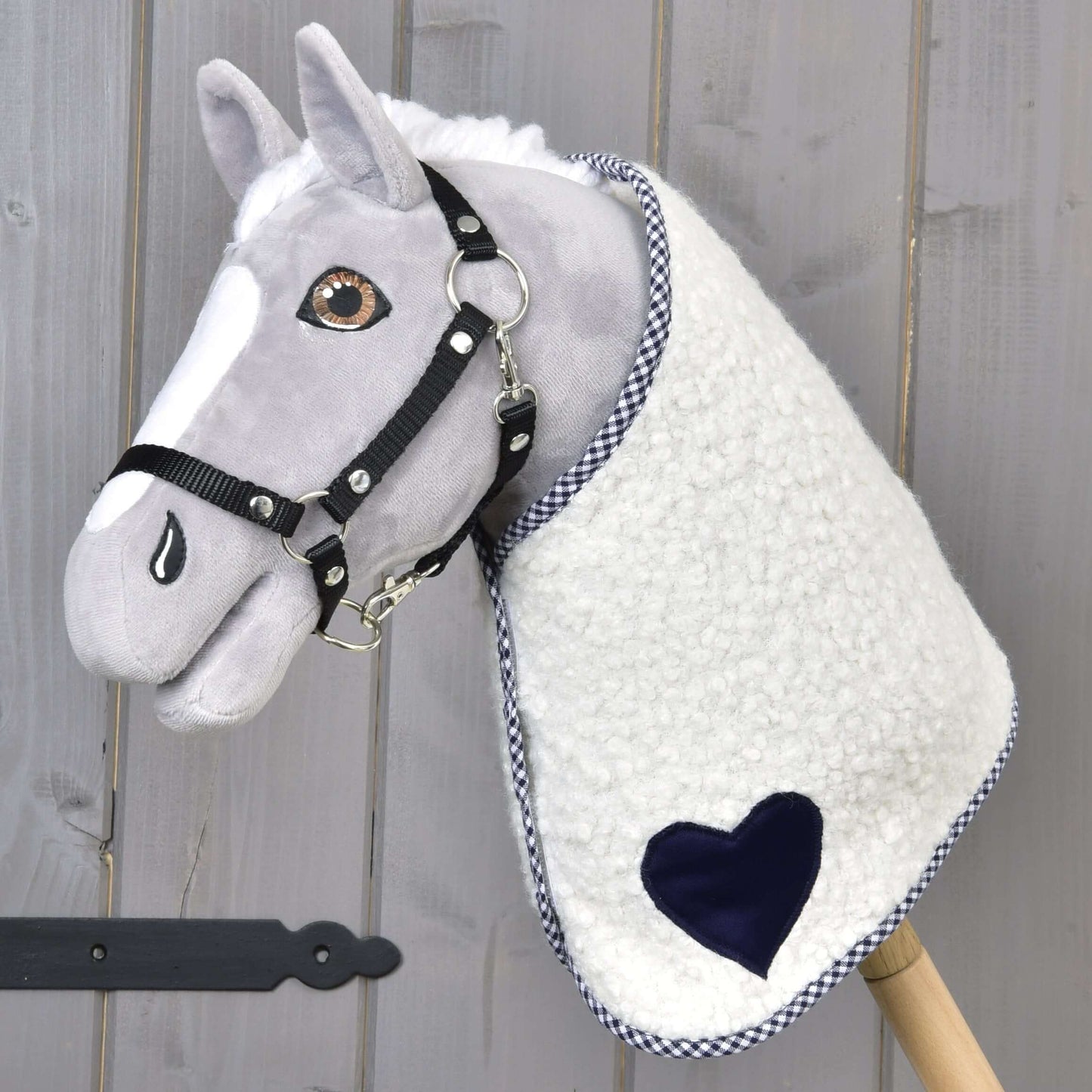 Deka Cube Blue od Hobby Horse LarDen na plyšovom Hobby Horse so sivou tvárou, čiernou uzdečkou a dekou s modrým akcentom, nasadenom na drevenej tyči, na drevenom pozadí.