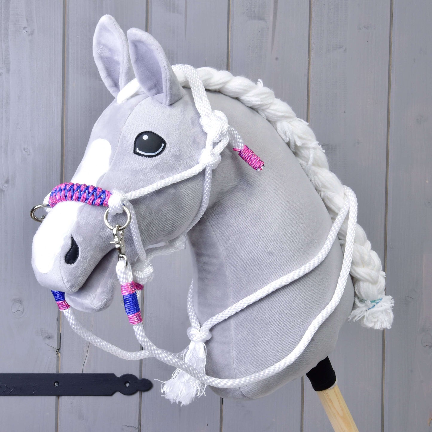 Povrazový set Biely (veľ. M) od Hobby Horse LarDen na sivom plyšovom Hobby Horse s bielou hrivou, opratami a pletenou ohlávkou s ružovými a modrými akcentmi, na drevenom pozadí.